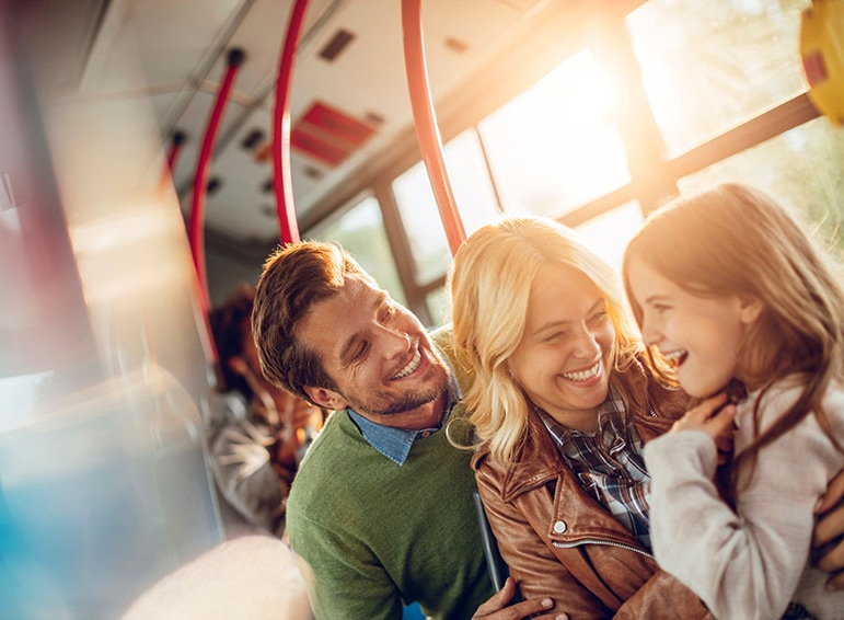 A family smiling and laughing, sitting on the bus with a bright, sunny background.